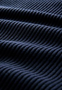 Tissu en velours côtelé bleu foncé avec des côtes verticales moelleuses et une texture douce, présenté en gros plan avec de la lumière créant des ombres sur les plis.