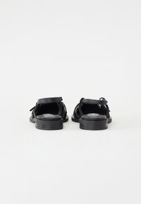 Schwarze Wildledersandalen mit flacher Sohle, offenem Rücken und dekorativen Bändern. Strukturiert Oberfläche mit einem glatten Fußbett.