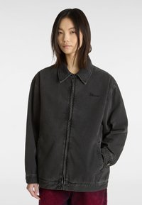 Zwarte denimjas met een puntige kraag, ritssluiting aan de voorkant en zijzakken. Beschikt over een subtiel geborduurd logo op de borst.