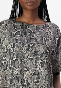 Kortärmad topp i ormskinnsmönster; har en svart och krämfärgad färgskala med strukturerade mönster och en oversized, avslappnad passform.