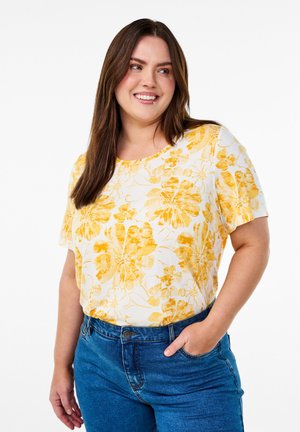 Kortærmet blomsterbluse med gule blomster på hvid baggrund, lavet af letvægtsstof, sat sammen med blå denim jeans.