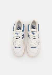 Pár bílých a modrých tenisek New Balance 550 pohledem shora na jednoduchém bílém pozadí, ukazující detaily šňůrek a loga.