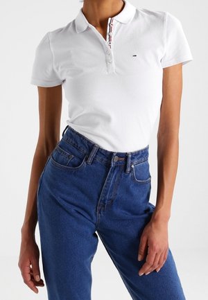 Biała bawełniana koszulka polo z plisą na trzy guziki, ozdobiona czerwonymi i granatowymi akcentami, zestawiona z wysokim stanem niebieskich dżinsów.