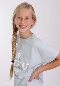 Lichtblauwe katoenen t-shirt met korte mouwen, voorzien van zilver metallic tekst "LAAT JE DROMEN STRALEN." Draag het met een lange gevlochten haarstijl.