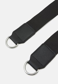 Cinghia in tessuto nero con accenti in pelle e anelli D in metallo argentato a ciascun estremo. Presenta una finitura testurizzata e cuciture robuste.