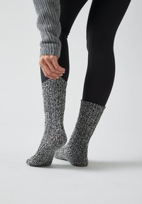 Calcetines de punto en blanco y negro, con textura de canalé y longitud hasta la mitad de la pantorrilla, exhibidos sobre una pierna junto a leggins negros.