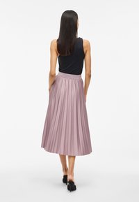 Záhybová midi sukňa vo svetloružovej farbe s priliehavým pásom. Skombinovaná s jednoduchým čiernym topom bez rukávov a čiernymi lodičkami na vysokom opätku.