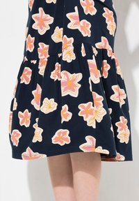 Abito navy con maniche corte, caratterizzato da grandi motivi floreali rosa e bianchi, una gonna a strati e una texture in tessuto morbido e leggero.