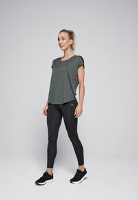 Donkergroene sporttop met korte mouwen, relaxte pasvorm, gecombineerd met zwarte high-waisted legging en zwarte sportschoenen. Eenvoudig ontwerp, gladde textuur.