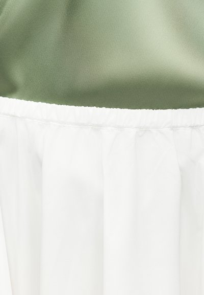 Κοντινό πλάνο λευκής ελαστικής μέσης κάτω από πράσινο ύφασμα, με έμφαση στην υφή και τις λεπτομέρειες ραφής.