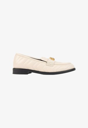 Mocassin en cuir matelassé couleur crème avec semelle noire et petite boucle dorée sur le dessus.