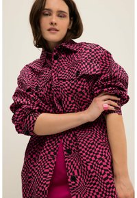 Camisa chaqueta de cuadros rosa y negra con cierre de botones, grandes bolsillos y mangas fruncidas. Usada sobre una prenda rosa.