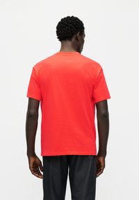 Κόκκινο βαμβακερό μπλουζάκι με κοντά μανίκια, στρογγυλή λαιμόκοψη και ίσια ραφή στο τελείωμα. Λείο ύφασμα, μίνιμαλ σχεδιασμός, χωρίς ορατά λογότυπα ή σχέδια.