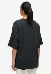 T-shirt nera oversize con maniche corte, tessuto di cotone, spalle abbassate e scollo rotondo, vista da dietro.