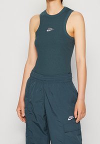 Tyrkysový žebrovaný top bez rukávů s malým bílým logem Nike a odpovídající volné cargo kalhoty s texturovaným povrchem a bočními kapsami.