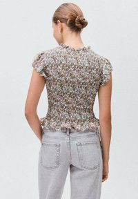 Blusa arricciata con motivo floreale in tonalità pastello e maniche a volant. Indossata con jeans a vita alta grigi chiari; vista posteriore mostrata.