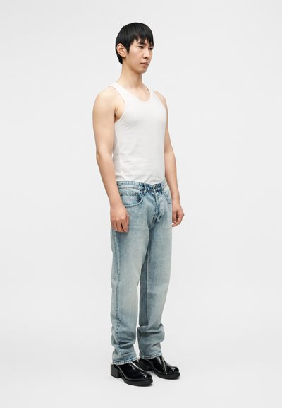 Ελαφρύ λευκό αμάνικο τοπ, ανοιχτό μπλε τζιν παντελόνι και γυαλιστερά μαύρα παπούτσια με τακούνι. Κανονική εφαρμογή και casual στιλ με ελάχιστες λεπτομέρειες.