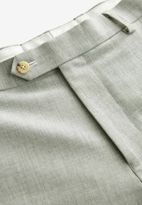 Pantalons taillés gris clair avec une texture lisse, un pli avant et une fermeture à un bouton à la taille.
