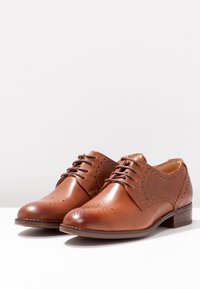 Chaussures oxford en cuir marron avec lacets, présentant des perforations décoratives, un bout arrondi et un petit talon empilé.