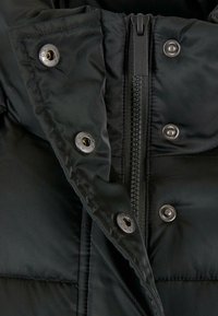Juodas pūkinis švarkas su užtrauktuku, metalinėmis detalėmis, matomu siuvimu ir sagų akcentais, demonstruojantis lygų, tekstūrinį paviršių.