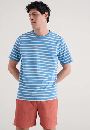 Kortebare T-shirt in lichtblauw met witte horizontale strepen. Ronde hals. Gecombineerd met koraalkleurige shorts. Zacht, katoenen materiaal.
