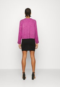 Maglione cropped fucsia a trama con maniche lunghe abbinato a una minigonna nera aderente e sandali neri con tacco.