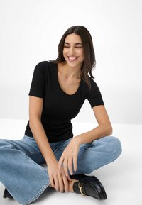 Sort kortærmet tætsiddende t-shirt med rund halsudskæring, parret med lyseblå vide ben jeans og sorte sko med detaljer i guldspænde.