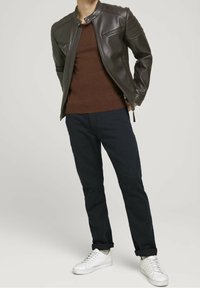 Bruine leren jack met gewatteerde details, gecombineerd met een brown sweater en donkere broek. Witte sneakers maken de outfit compleet.