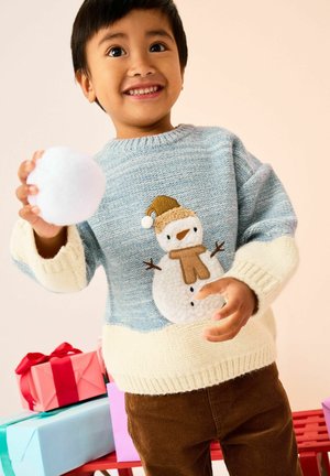 Junges Kind trägt einen Schneemann-Pullover und hält einen Schneeball mit verpackten Geschenkboxen im Hintergrund vor hellem Hintergrund.