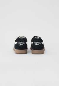 Fekete velúr sportcipők fehér kiegészítőkkel, Reebok logóval a saroknál, valamint egy bézs gumitalppal. Klasszikus sziluett és texturált anyag.