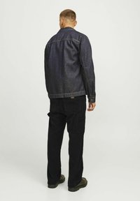 Donkerblauwe denim jack met een klassieke snit, voorzien van zichtbare stiksels en een kraag. Gecombineerd met zwarte corduroy cargobroeken.