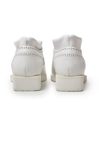 White leather shoes with a rounded toe, low block heel, and decorative perforated accents on the back and sides. Smooth surface texture.