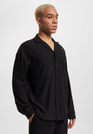 Black striped button-up shirt with a relaxed fit, short collar, and two front pockets. Soft fabric gives a smooth texture.