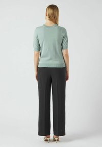 Minta zeleni pulover kratkih rukava s okruglim izrezom, uparen s crnim hlačama širokih nogavica visokog struka, koji prikazuju glatku teksturu.