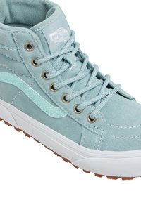 Lichtblauwe suède high-top Vans sneakers met een witte rubberen zool, blauwe veters, metalen oogjes en een glinsterende lichtblauwe golfstripe.