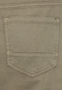 Μπεζ τζιν τσέπη με υφή, στρογγυλεμένες γωνίες και αντίστοιχο κέντημα σε ανοιχτό ύφασμα φόντου.