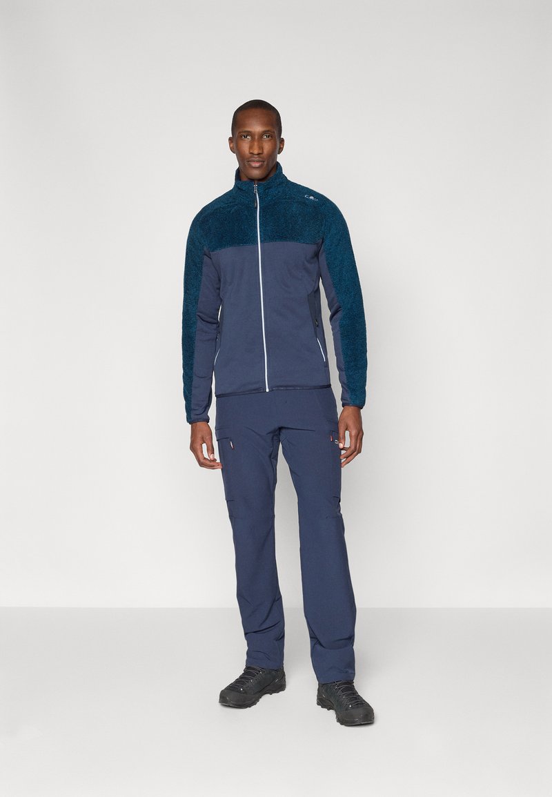 Granatowa kurtka polarowa z zamkiem z przodu, z teksturowanym górnym materiałem i gładkim dolnym. Połączona z pasującymi spodniami.