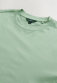T-shirt de algodón verde claro con cuello redondo y mangas cortas. Presenta una etiqueta en el cuello con información de la marca y la talla.