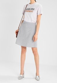 T-shirt en coton violet clair avec l'inscription « SUPERLATIVE CONSPIRACY », associée à une jupe trapèze grise à rayures et des chaussures à talons argentées.