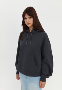 Mørk grå hettegenser med romslig kengurulomme, snor til hetten og avslappet passform. Kombinert med lys blå denimskjørt. Myk tekstur.