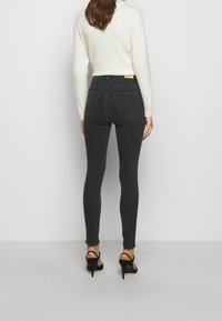 Jeans skinny negros de cintura alta con una textura suave y cuatro bolsillos. Combinados con un suéter crema y tacones negros con tiras.