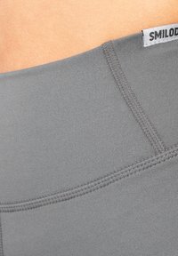 Grijze legging met een gladde textuur, voorzien van een brede tailleband en platte naden voor comfort. Merkenlabel "SMILODON" zichtbaar aan de bovenkant.