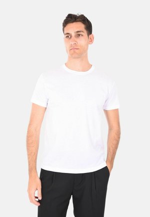 T-shirt in cotone bianco con scollo rotondo e maniche corte, indossato da un modello maschile in pantaloni neri. Superficie liscia, senza motivi.