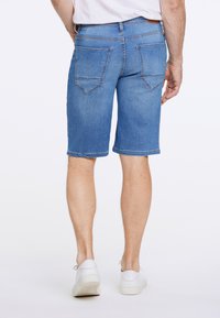 Farkkushortsit vaaleansinisinä, suoran leikkauksen, ommeltujen takataskujen ja huolitellun reunan kanssa. Yhdistettyinä valkoisten lenkkareiden kanssa.