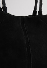Sac cabas en daim noir avec deux poignées en cuir enveloppées et des coutures verticales visibles sur le panneau avant.