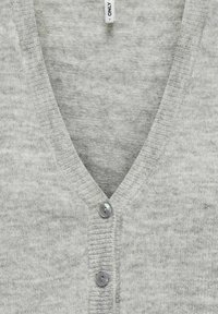 Cardigan en tricot gris clair avec col en V, deux boutons sur le devant et une étiquette de vêtement blanche visible portant la mention "ONLY" près de l'encolure.