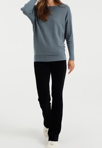 Jasnoniebieski sweter w prążki z długimi rękawami, zestawiony z czarnymi spodniami z kordurowej tkaniny i białymi sneakerami, na jednolitym tle.