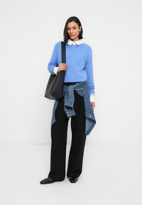 Pull bleu clair, chemise blanche à col, jean noué à la taille, pantalon large noir, sac fourre-tout noir et chaussures noires brillantes.