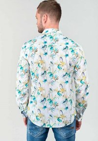 Witte blouse met lange mouwen, versierd met een meerkleurig bloemenpatroon in tinten blauw, groen en geel; knoopsluiting aan de kraag, rechte zoom.