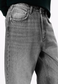 Harmaa denim-farkut, joissa on kulunut pinta, klassinen viiden taskun muotoilu ja hienovarainen rakenne. Varustettu napilla ja vetoketjulla.